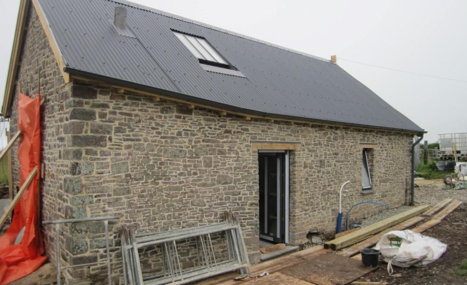 The barn conversion nearing completion with agricultural style corrugated roof, repointed stonework and dark metal window and door frames. Photo courtesy of Hiax Preservation